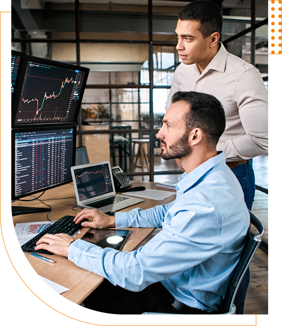 Two men analyzing financial charts on multiple monitors in a modern office setting.