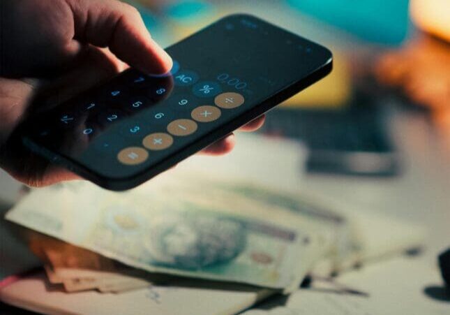 Hand using smartphone calculator with currency notes
